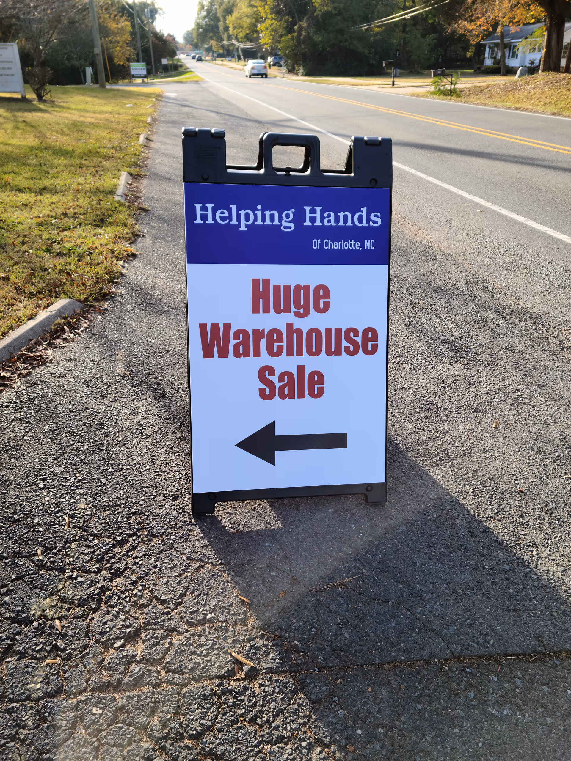 Foreground road sign advertising Helping Hands warehouse sale with arrow on a street.
