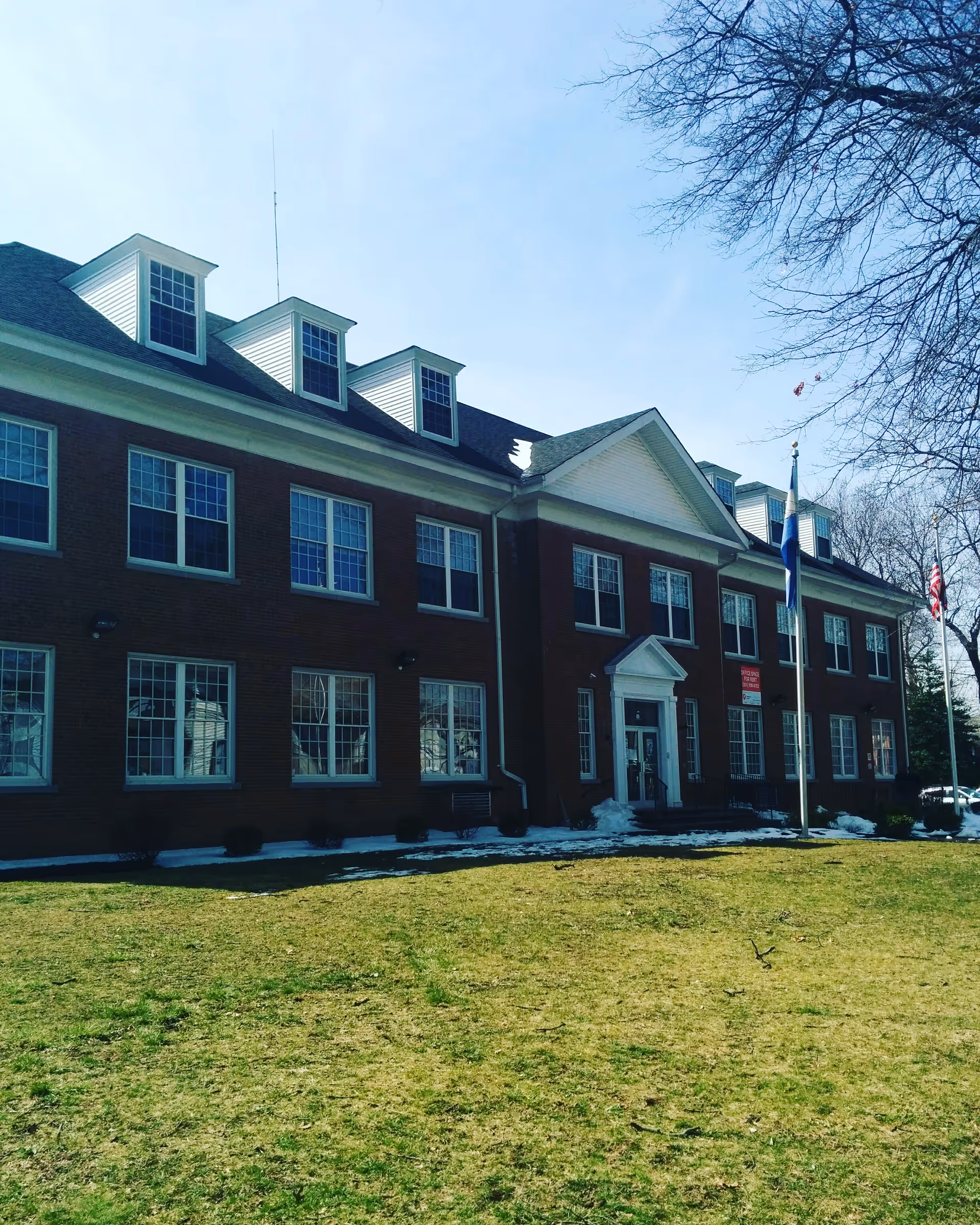 Red brick senior living facility facade with white trim, gabled roof, and flags on the lawn.