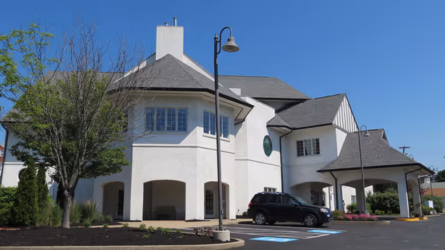 White hospice building with arches, a parked car, and a clear blue sky.