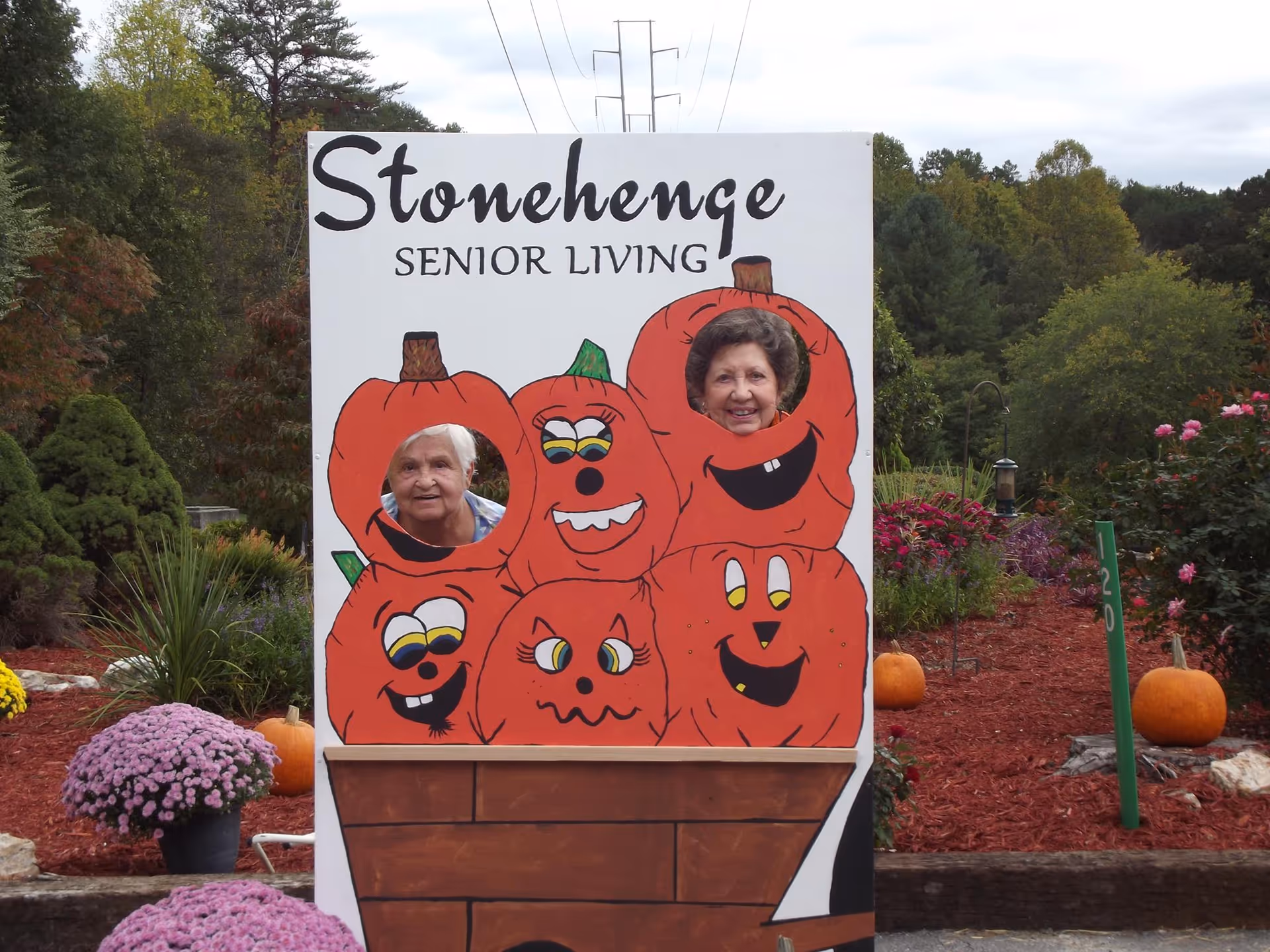 Exterior Stonehenge Senior Living sign with two residents peeking through pumpkin-cutout holes.