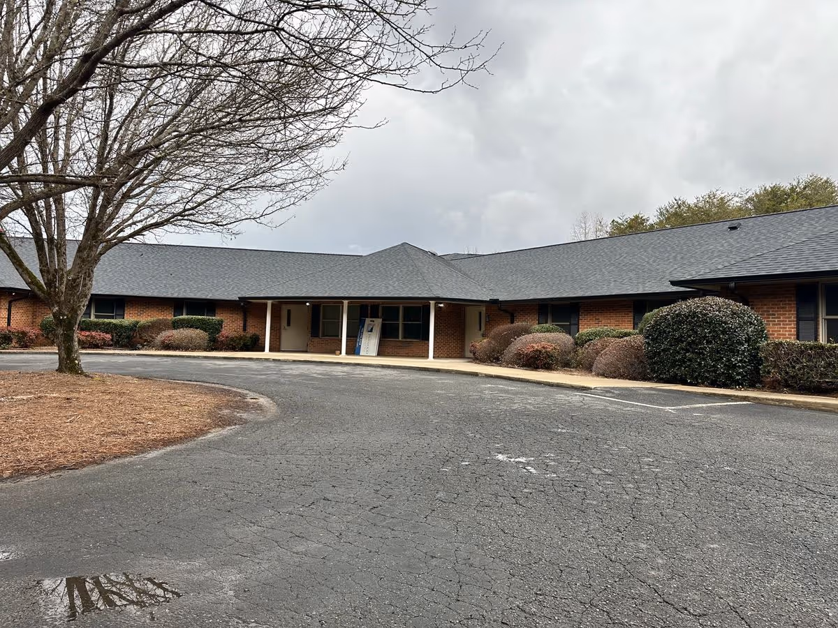 Front view of a single-story brick senior living building with a covered entrance, circular driveway, and shrubs.