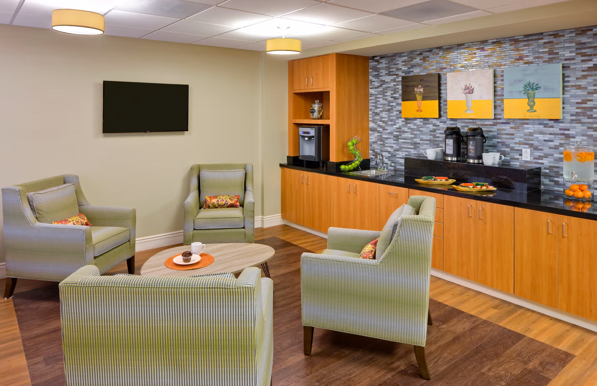 Bright lounge in a care facility featuring green striped chairs, coffee station, and wall art.