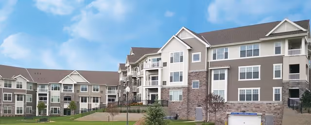 A large multi-story senior living facility with beige siding, balconies, and stone accents.