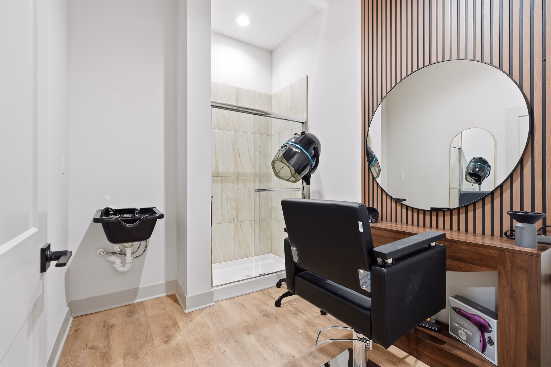 Hair salon station inside a senior living facility featuring a black chair, round mirror, and shower.