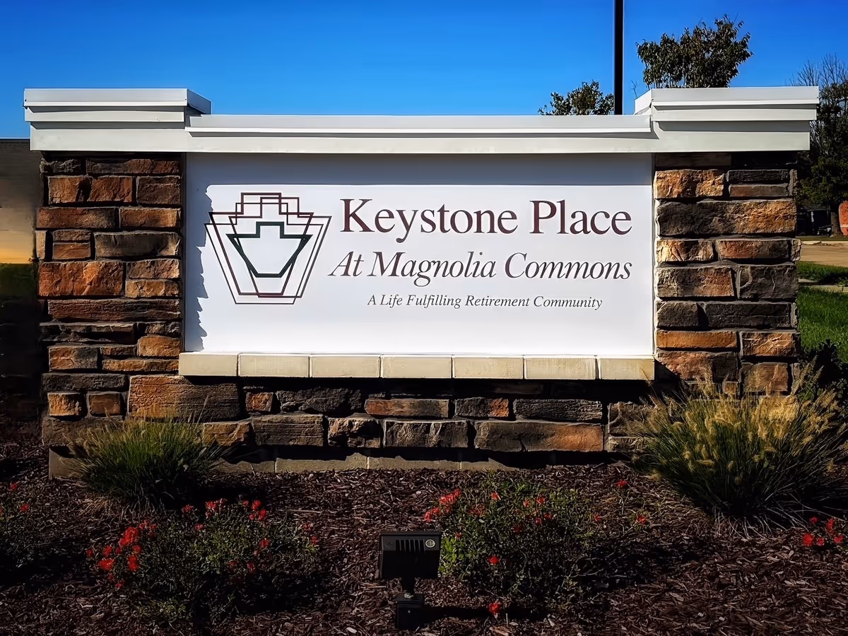 Stone entrance sign reading "Keystone Place At Magnolia Commons" set in a landscaped bed.