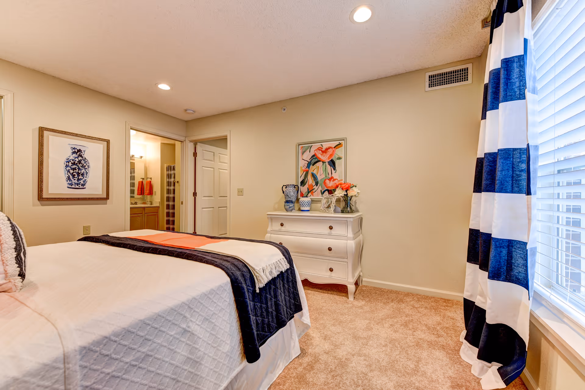 Cozy bedroom with a bed, white dresser, artwork, and striped blue curtains.