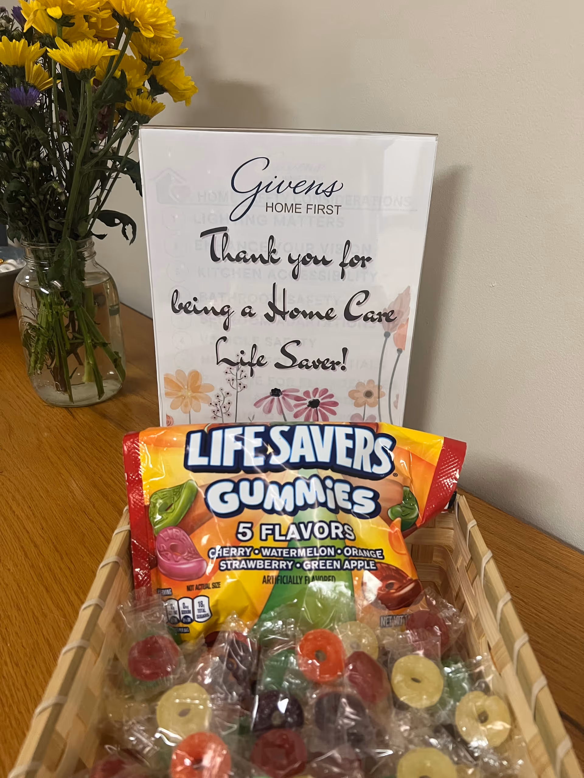 Vase of flowers and a Givens Home First sign beside Lifesavers Gummies on a table.
