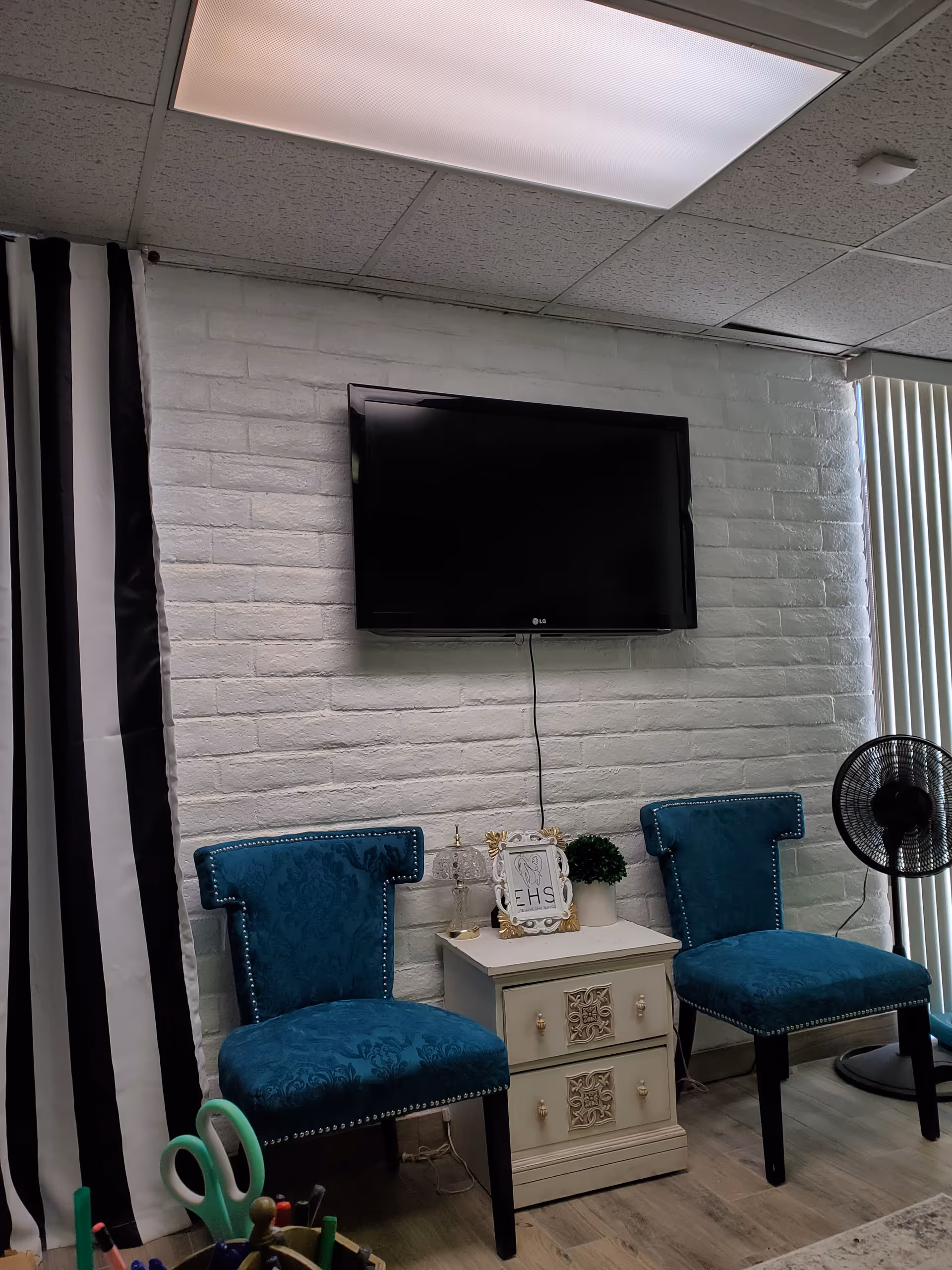 TV mounted on a white brick wall with blue upholstered chairs and a decorative dresser.