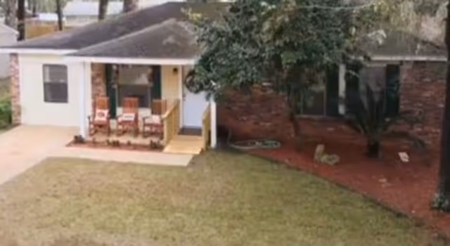 Front exterior of a single-story senior home with a small porch and chairs.