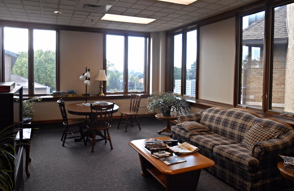 Common living room with a plaid sofa, coffee table, round table with chairs, and large windows.