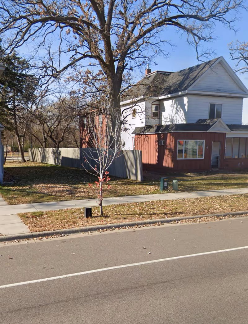 Two-story senior lodging home exterior with white upper, red lower walls, and a nearby tree.