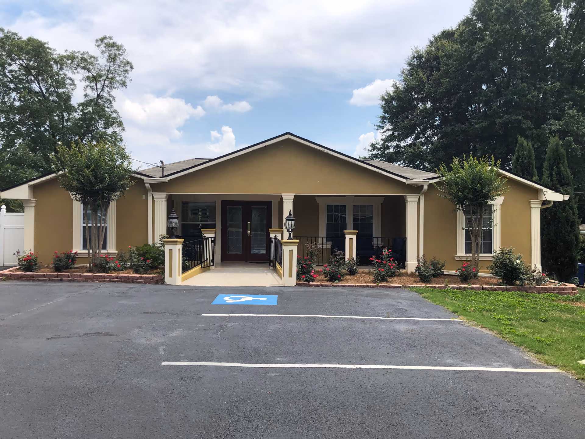 Single-story beige senior living facility front entrance with handicap parking and landscaping.