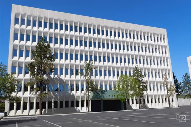 White multi-story building with grid of windows and trees in front