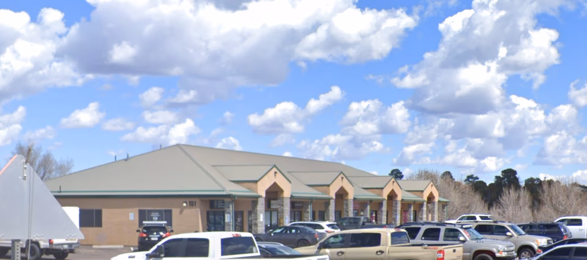 Single-story senior living facility front with beige brick, archways, and parked cars.
