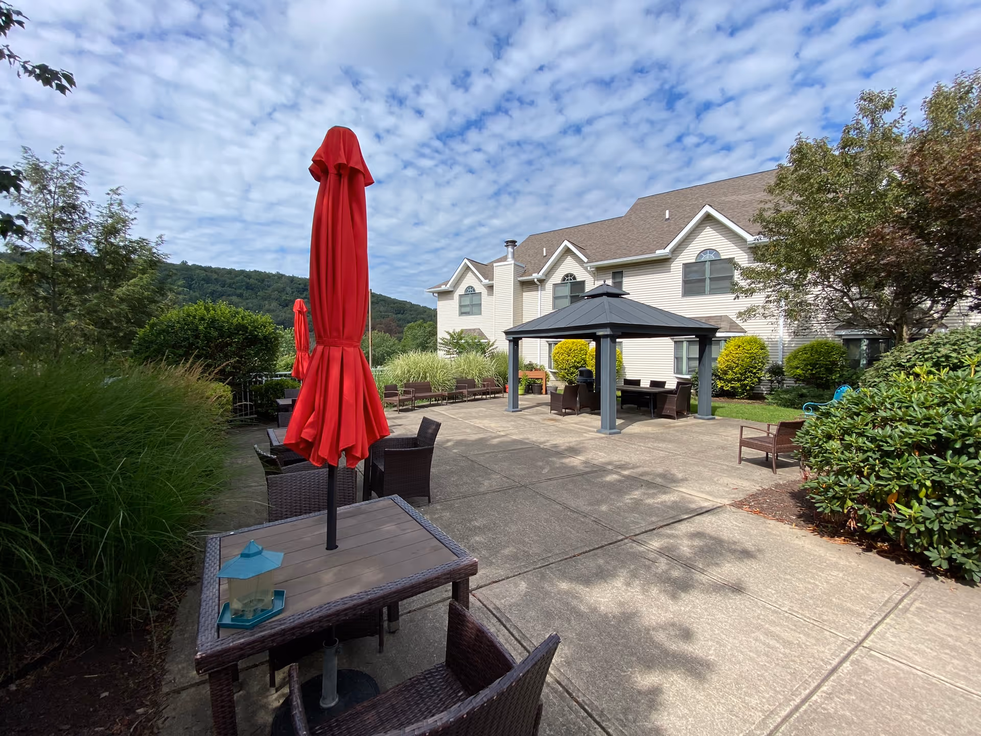 Outdoor patio area of Willowbrook Place with red umbrellas, tables, chairs, and a gazebo.