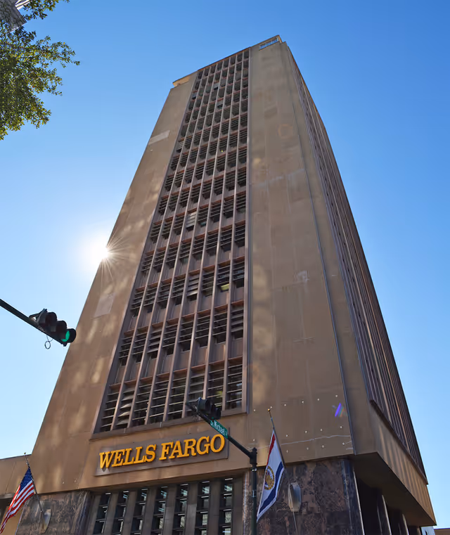 Tall Wells Fargo building with blue sky and flags.