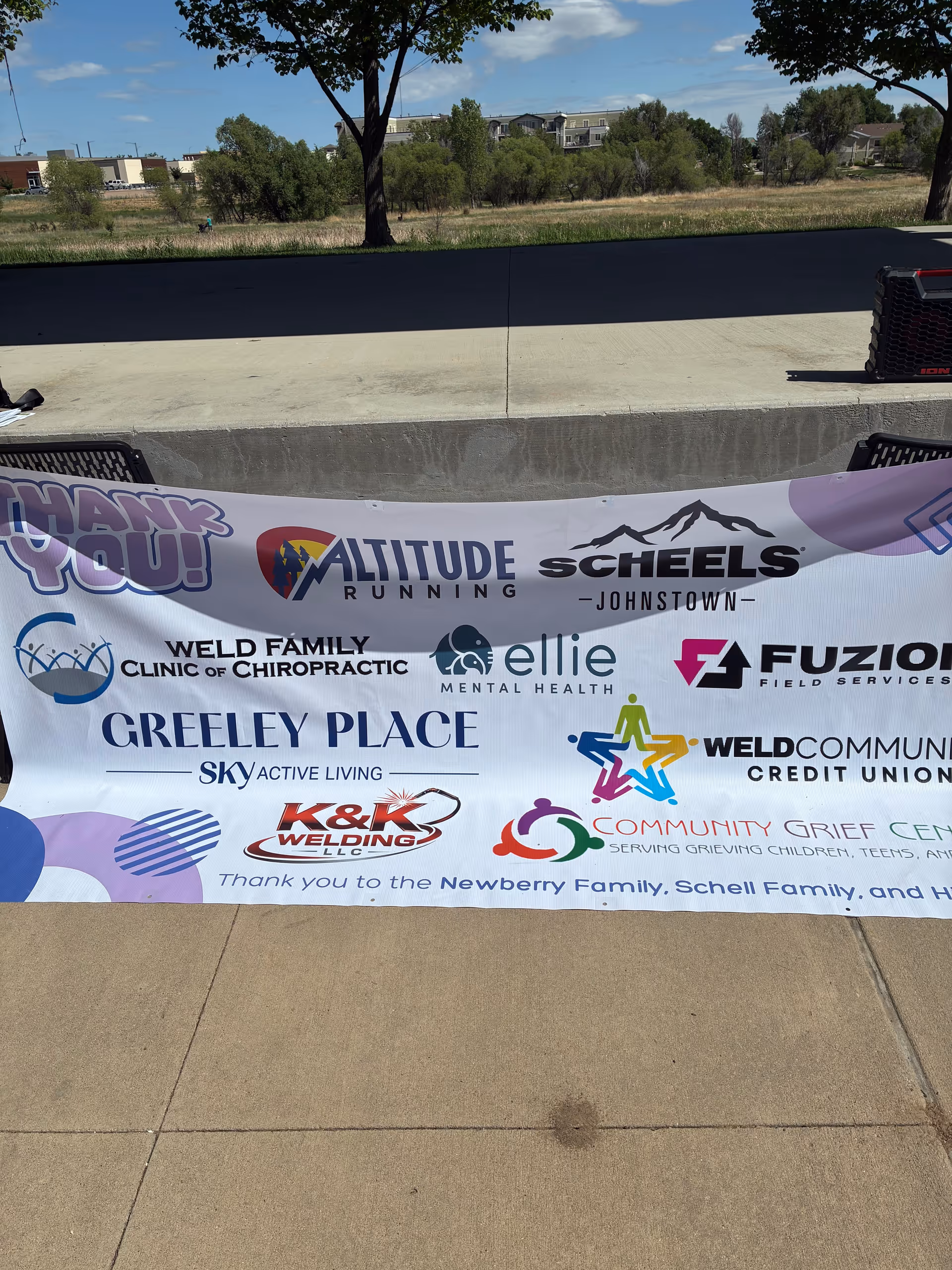 Outdoor banner display with multiple sponsor logos along a concrete walkway.