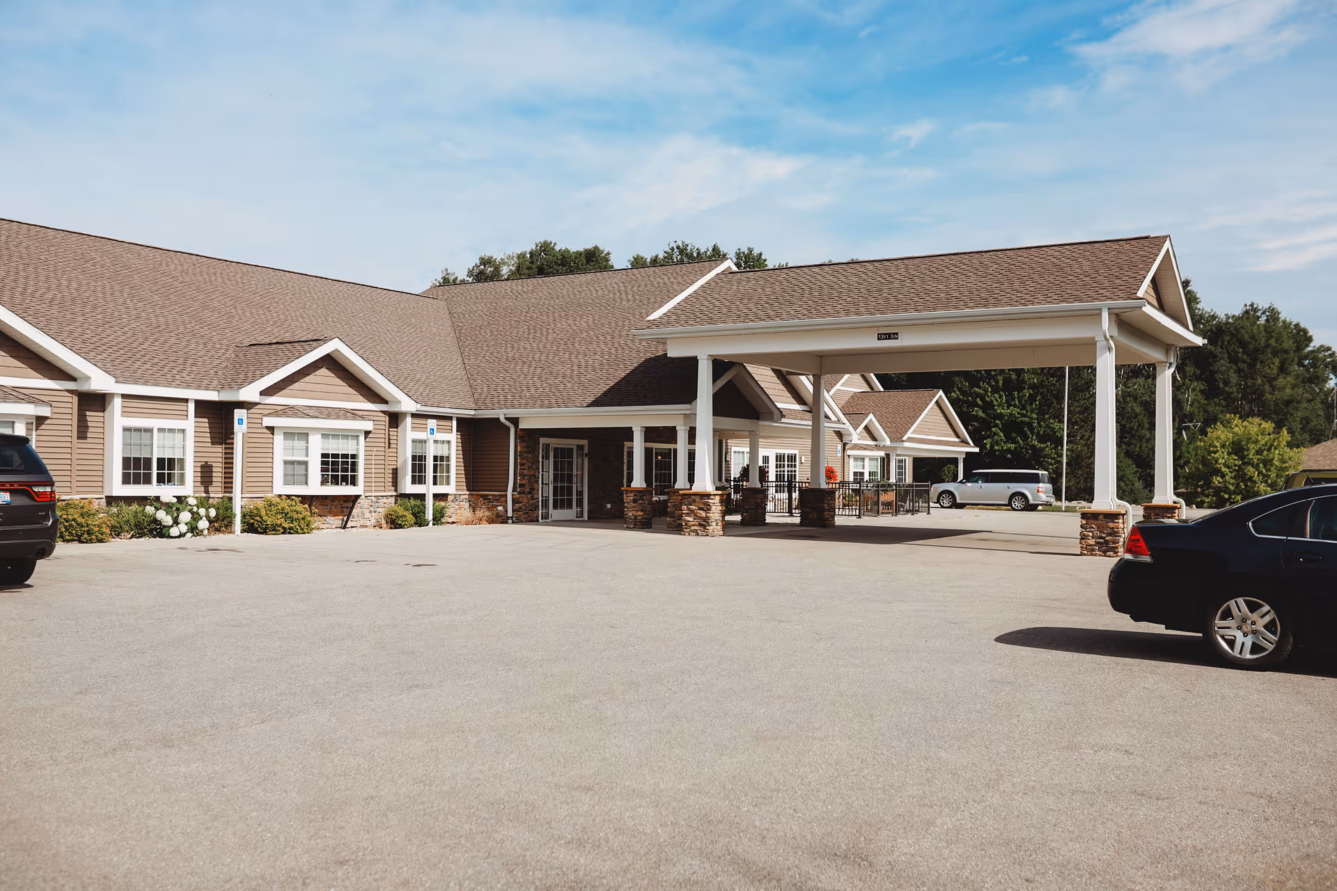 Exterior of a senior living facility with a covered entrance and parked cars.