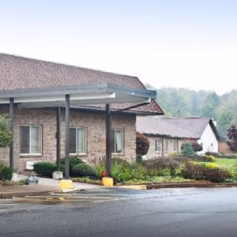 Brick senior living building with a covered entrance and surrounding shrubs under a cloudy sky.