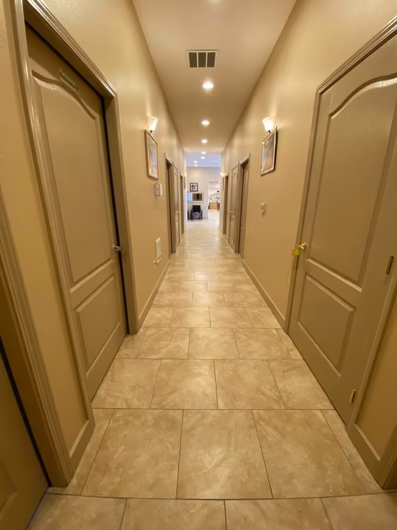 Long hallway inside a senior living facility, with doors along both walls and a tiled floor.