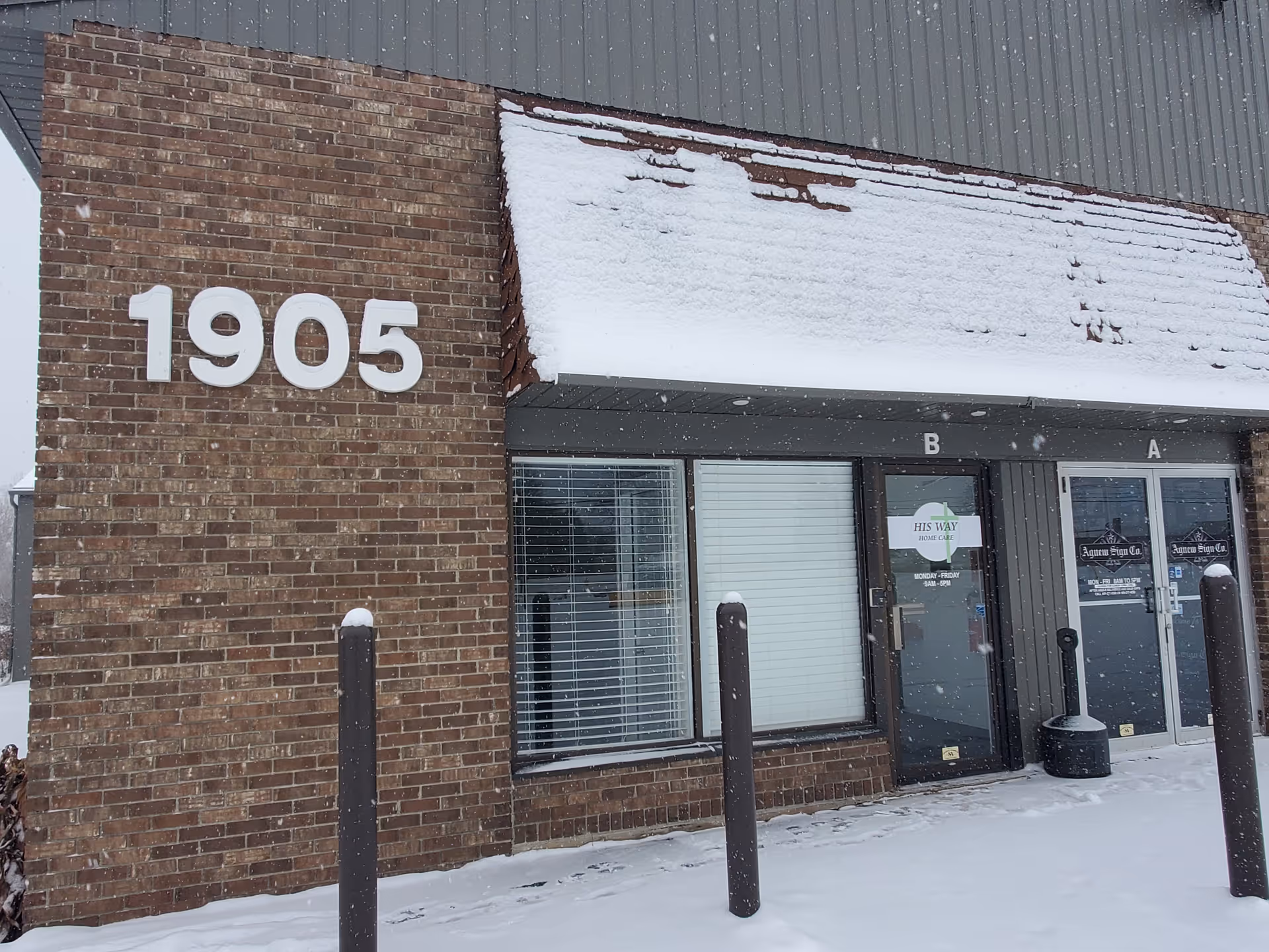 Snow covers the brick building front showing 1905 and doors with His Way Home Care sign.