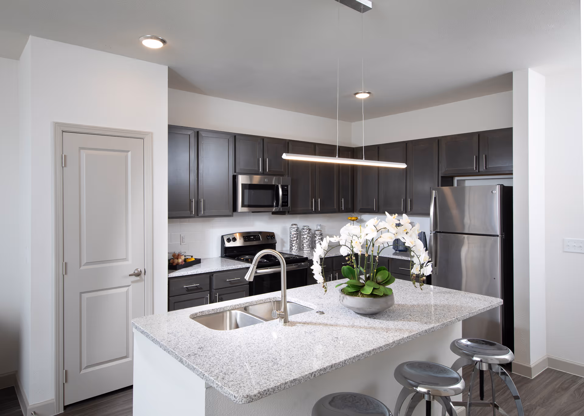 Modern kitchen with an island, dark cabinets, stainless appliances, and a potted orchid.