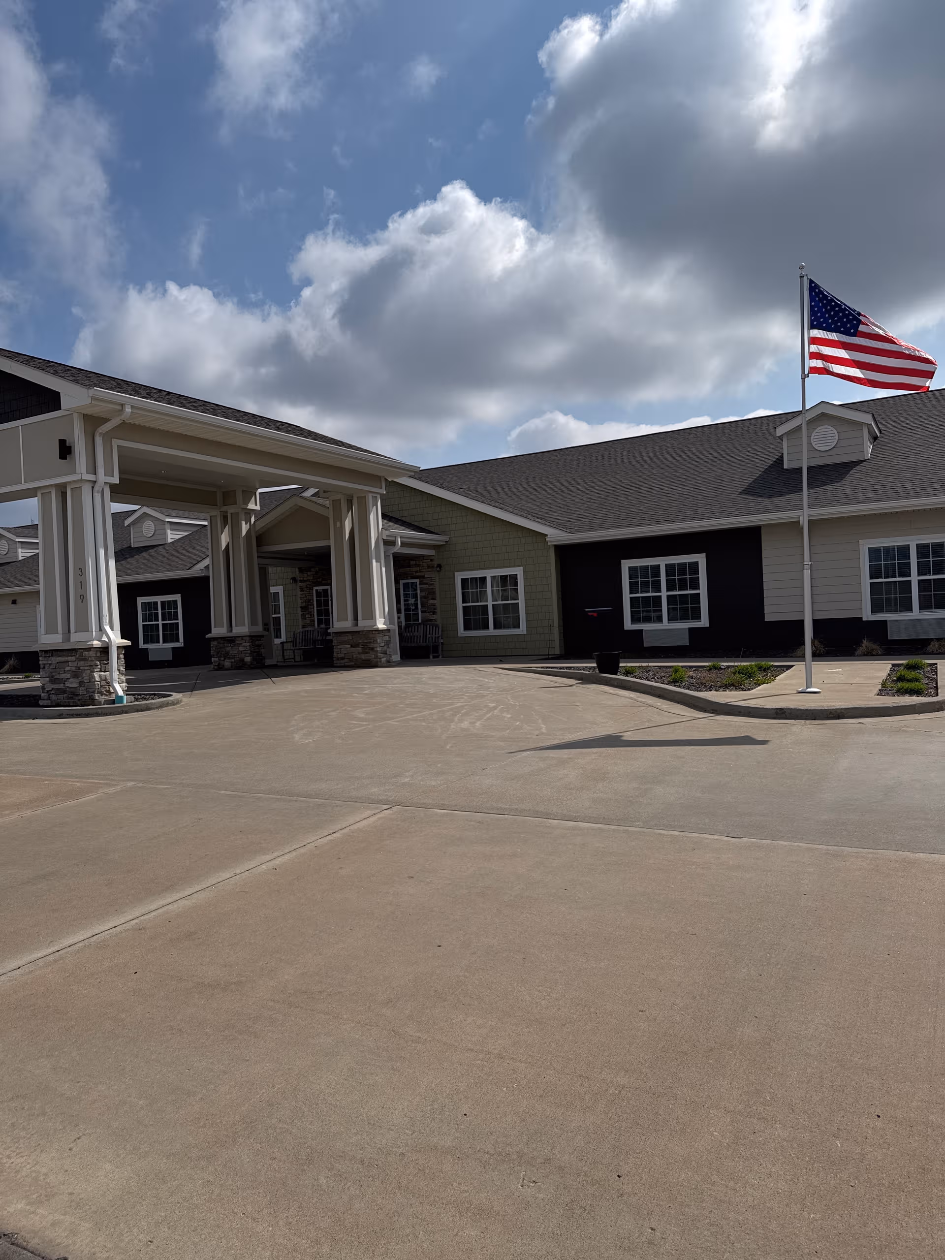 Exterior view of High Point Residence Quincy with entrance canopy, parking driveway, and American flag.