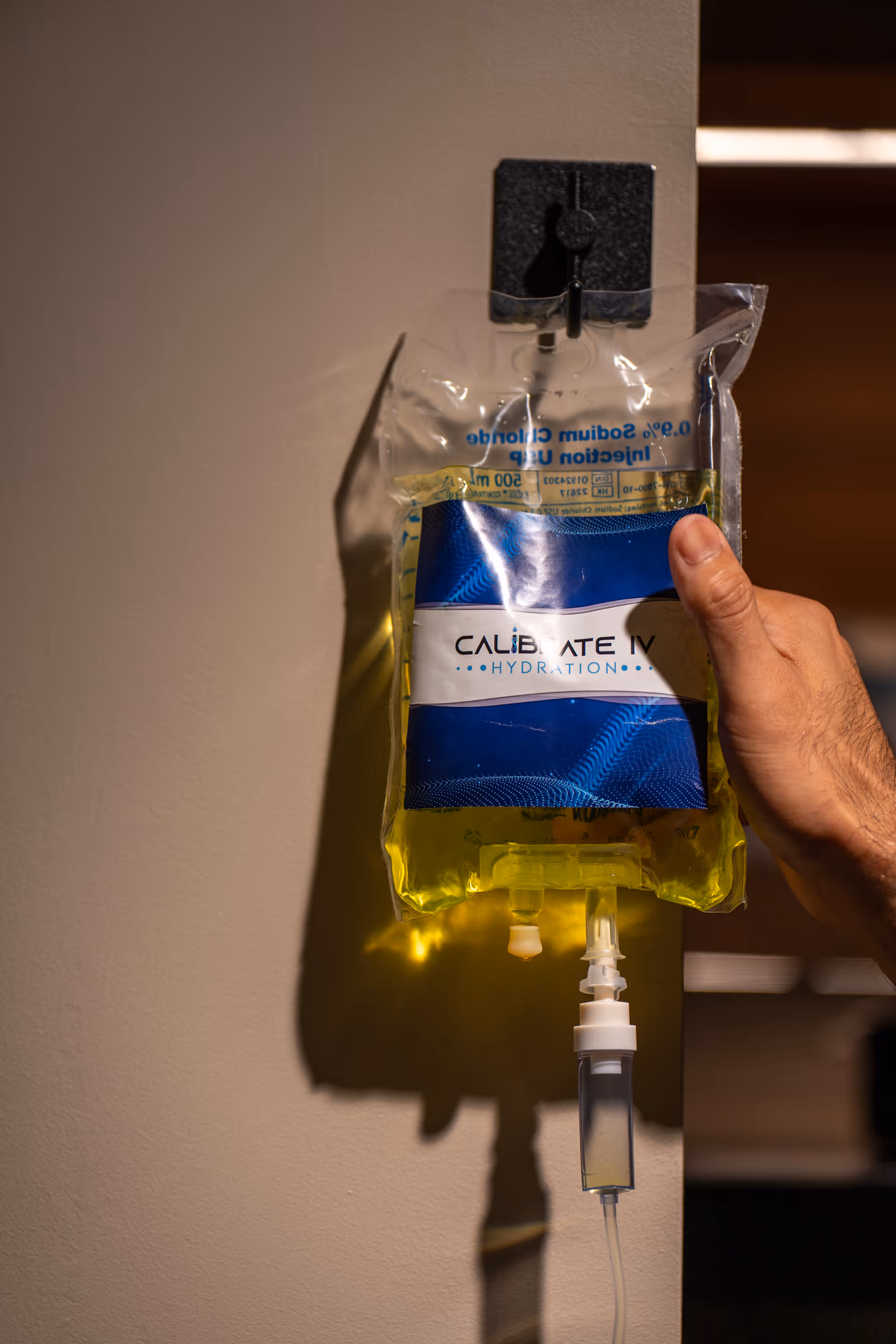 IV hydration bag labeled Calibrate IV hangs on wall with hand adjusting tubing