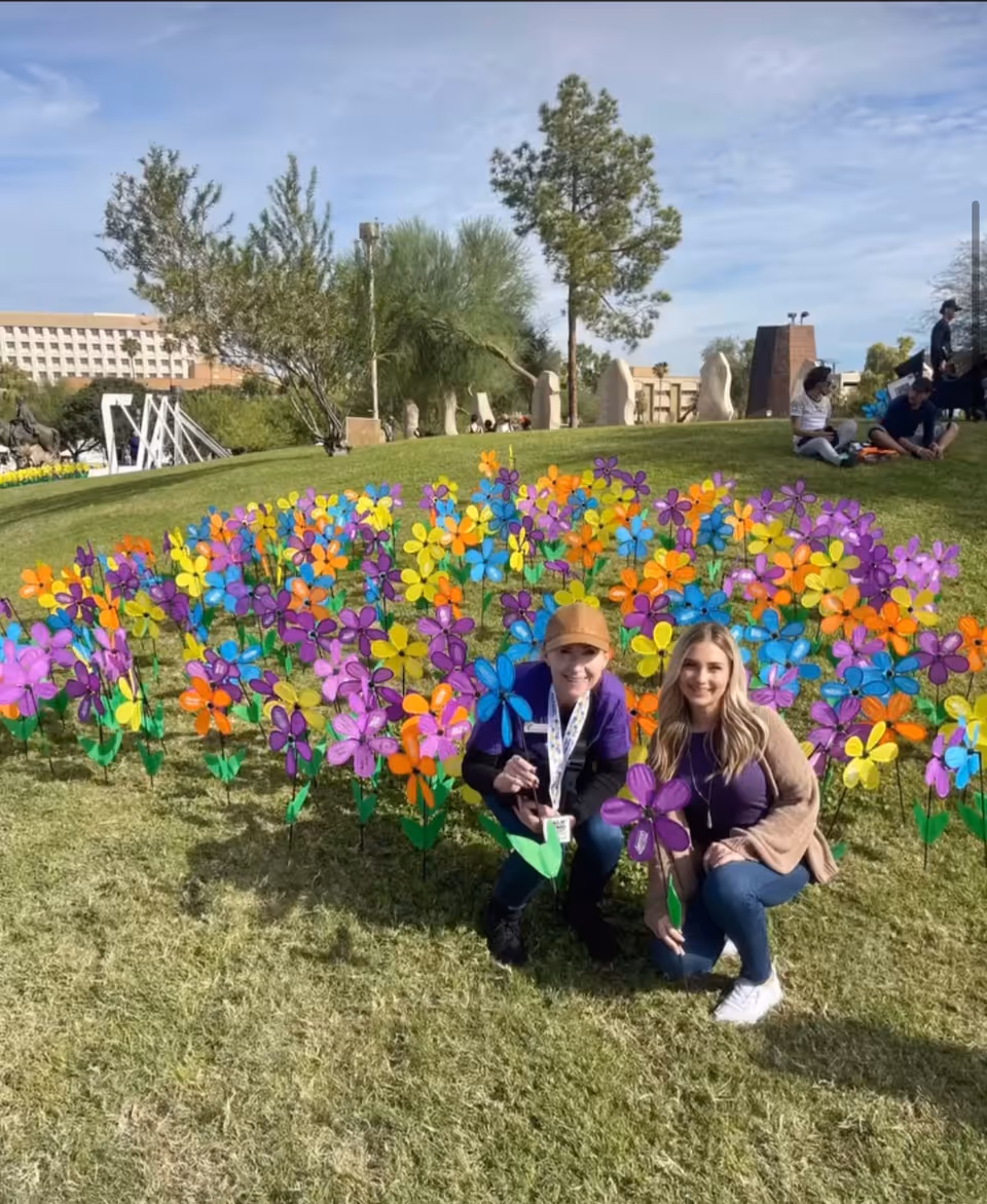 Two people kneel beside a colorful field of pinwheels in a sunny outdoor garden.