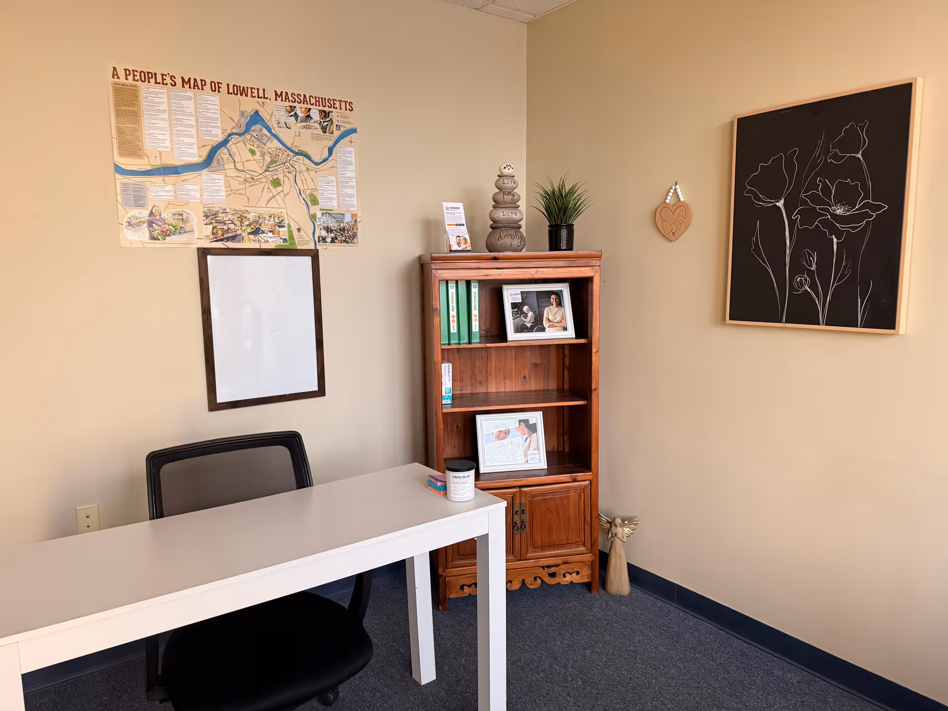 Office corner with white desk, black chair, wooden bookshelf, map poster, and wall art.