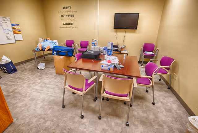 Conference room with a large table, purple chairs, wall art, and a wall-mounted TV.