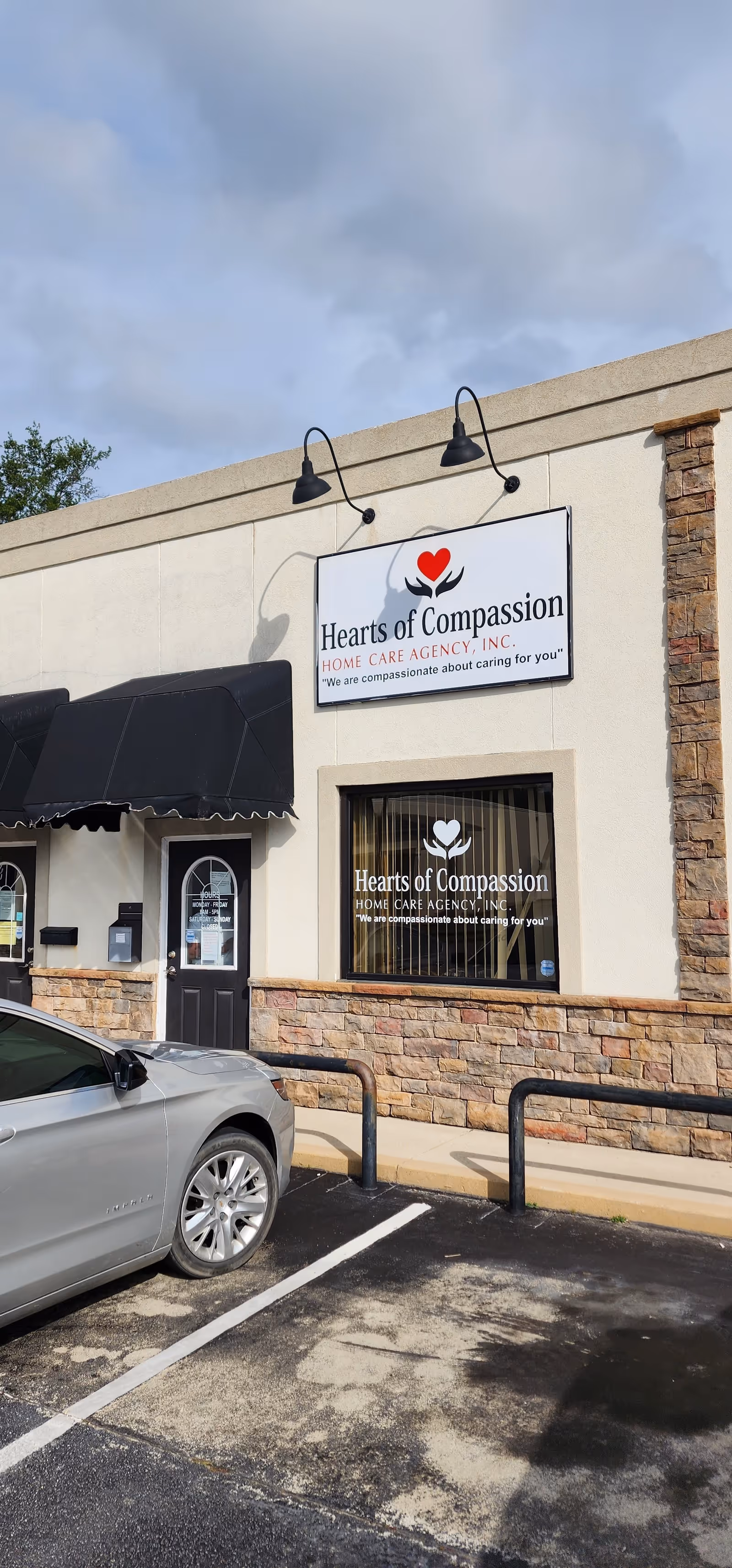 Exterior view of Hearts of Compassion facility with sign, storefront, and parked car.