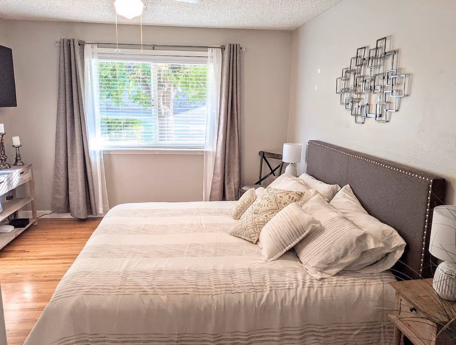 A neatly made bedroom with a large bed, pillows, nightstands, and a window with curtains.
