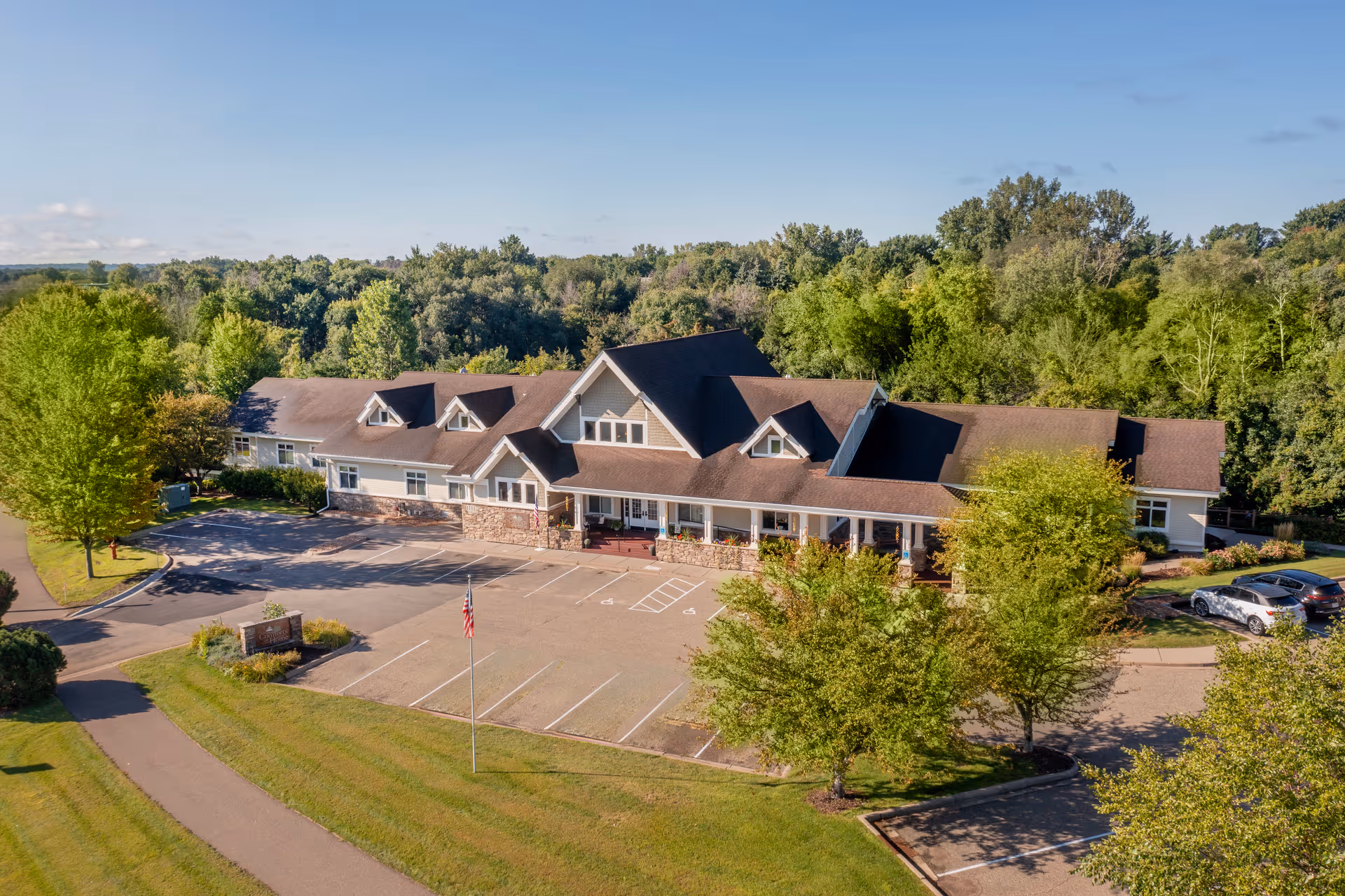 A multi-wing senior living facility with a sloped roof, parking lot, and surrounding trees.
