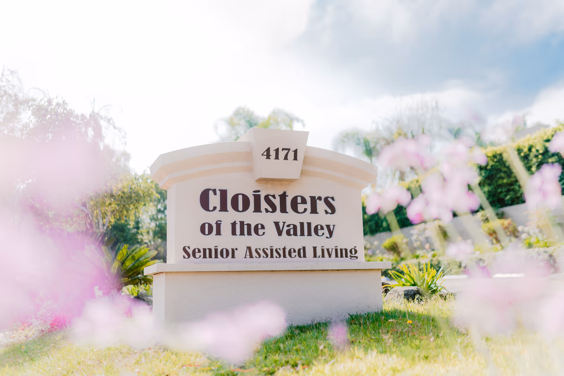 A stone sign for Cloisters of the Valley Senior Assisted Living with pink flowers in foreground.