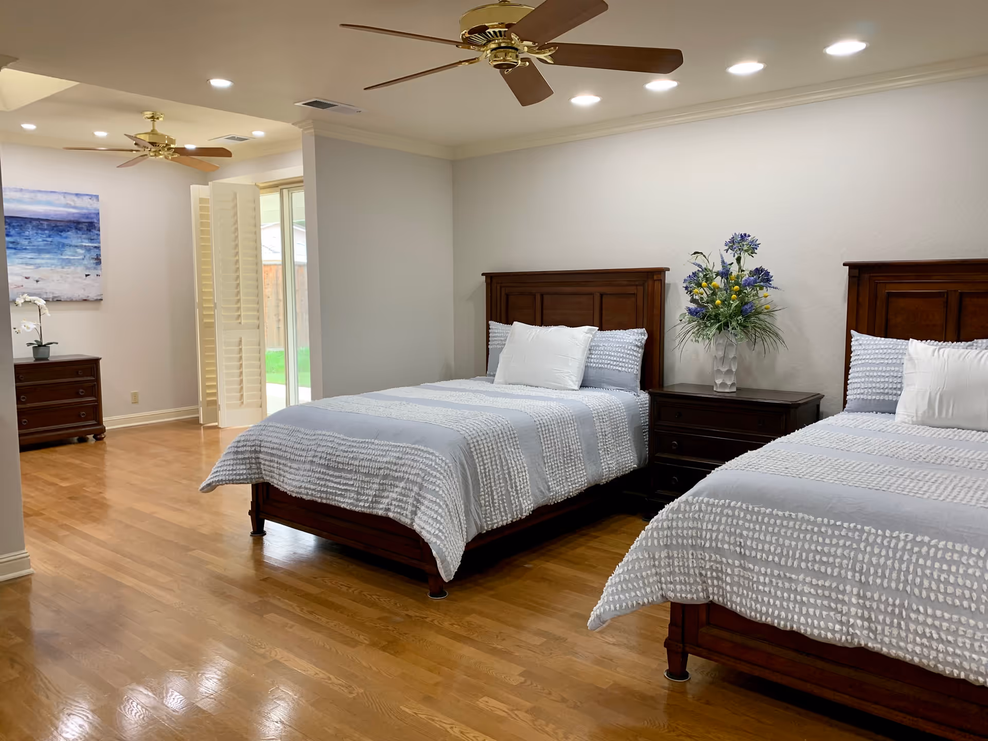 Two twin beds with dark wood headboards, nightstand, and a dresser in a bright bedroom.