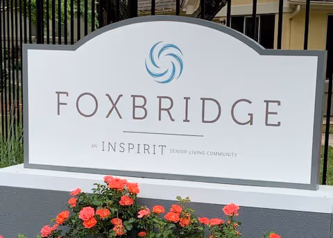 A large Foxbridge sign with a blue circular logo and blooming flowers in front.