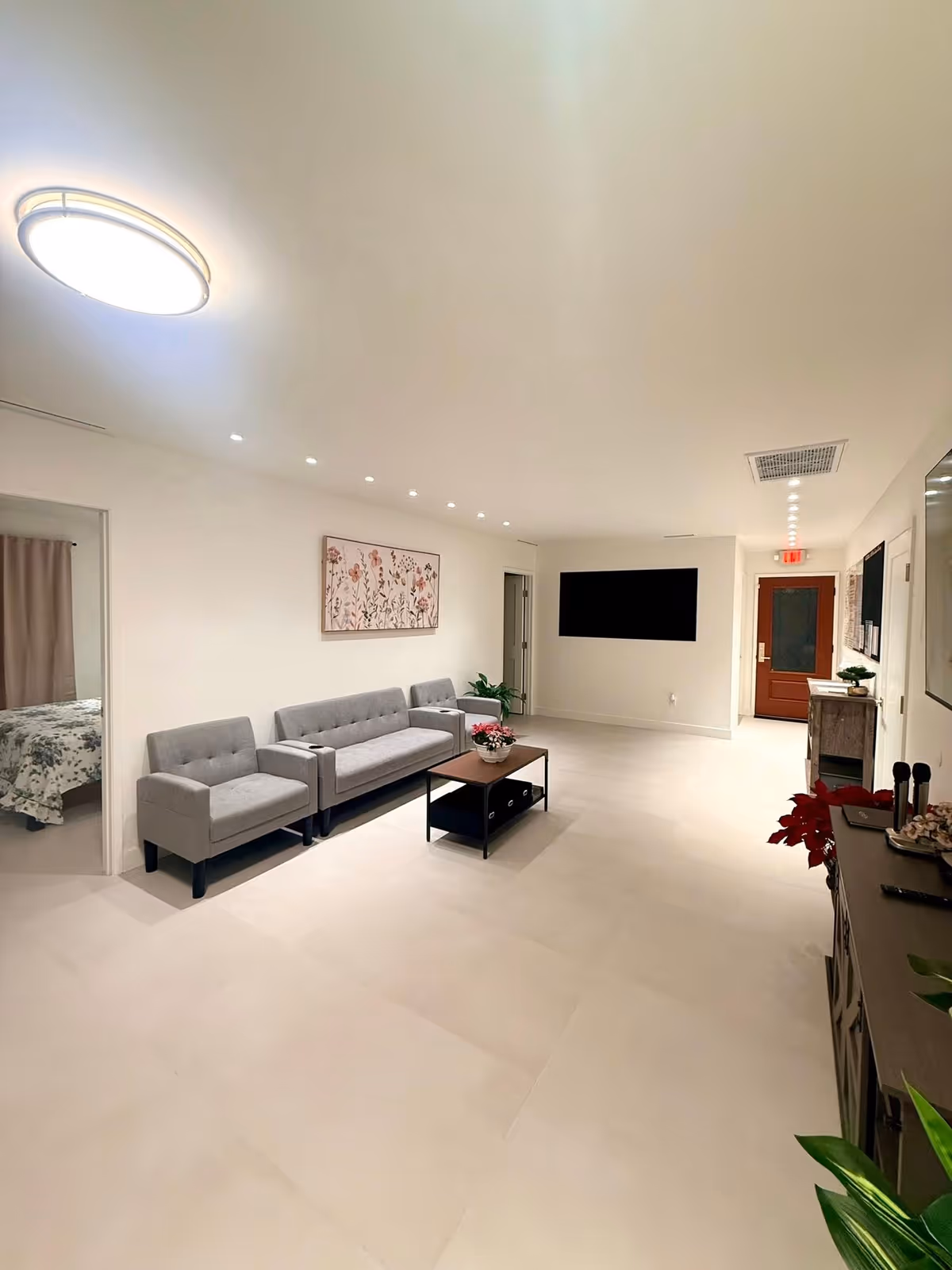 Bright, modern lounge with gray couches, coffee table, and wall-mounted TV in a senior living facility.
