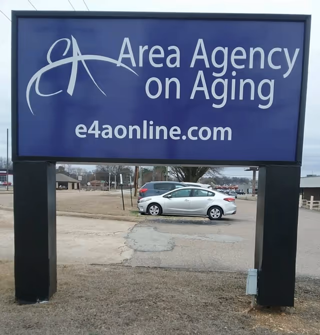 Large blue exterior sign reading Area Agency on Aging with a parked car behind.