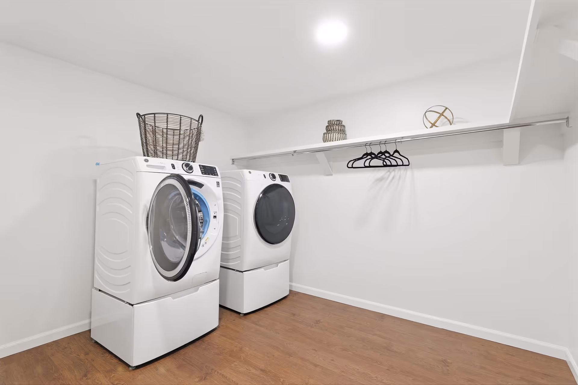 Laundry room with two front-loading washers, a shelf, and hanging rack.