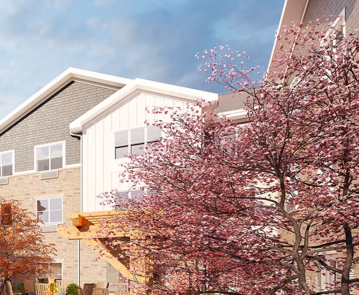 Exterior view of a multi-story senior living building facade with pink flowering trees and an outdoor wooden pergola.