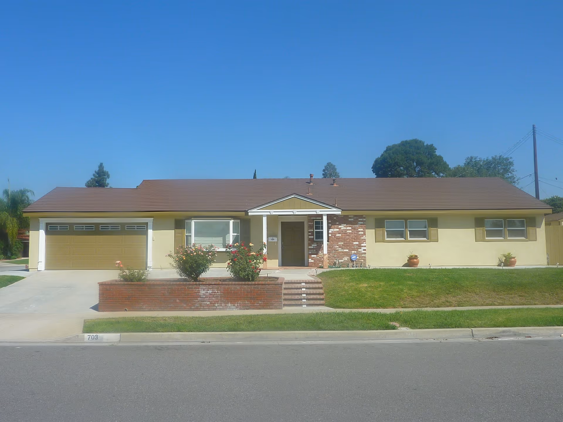 Front view of a single-story beige house with brown roof, garage, and lawn.