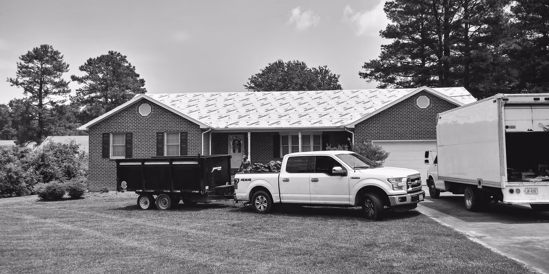 Brick facility with a driveway, pickup, trailer, and a moving truck parked out front.