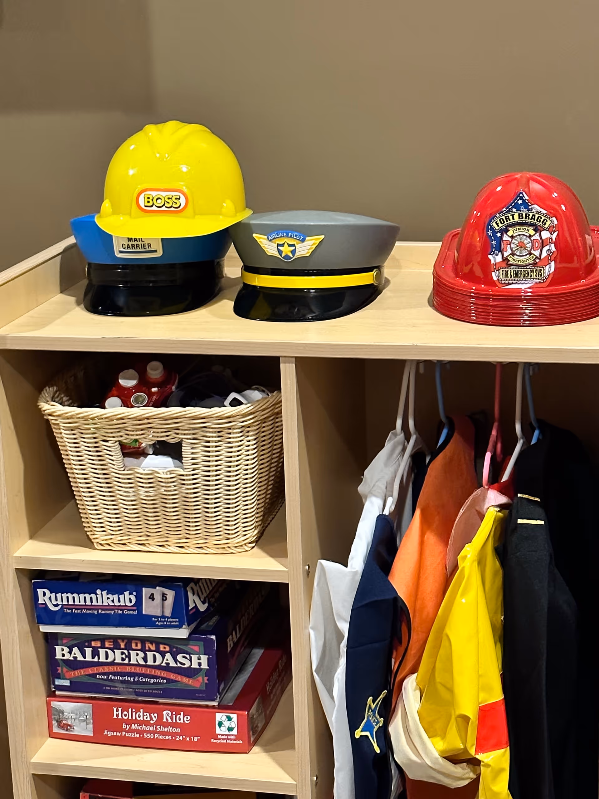 Indoor storage cubbies with firefighter hats, a woven basket, coats, and board games.