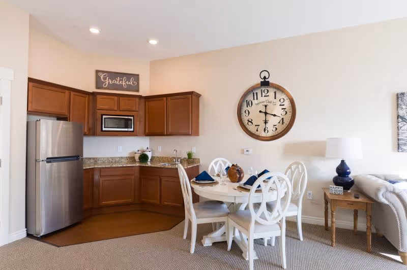 Open-concept kitchen and dining area with wooden cabinets, stainless fridge, surrounding seating.