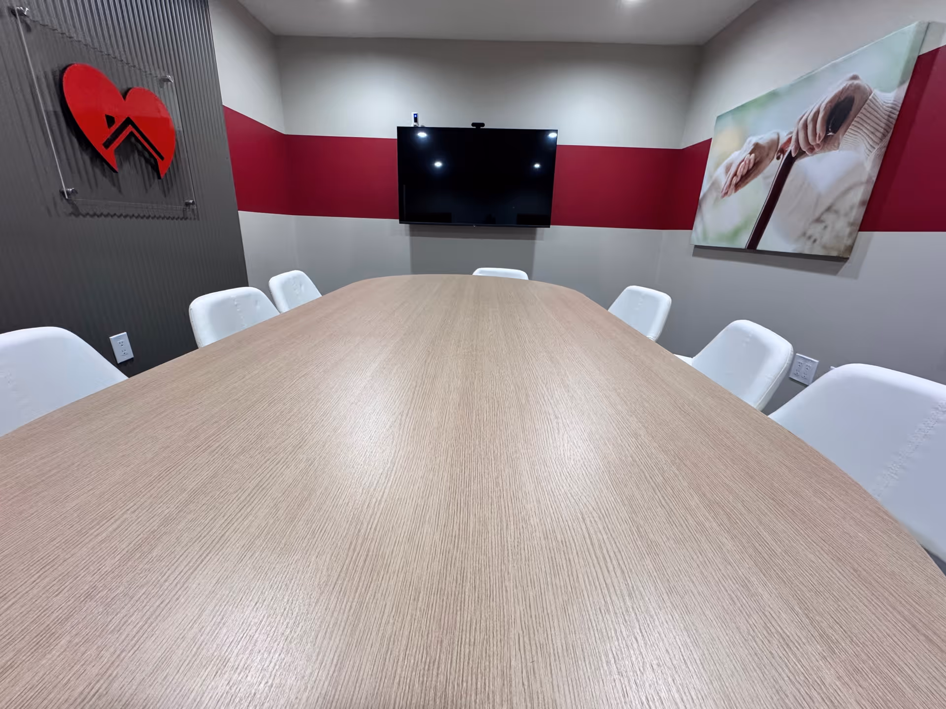 Conference room with a long wooden table, white chairs, and a wall-mounted TV.