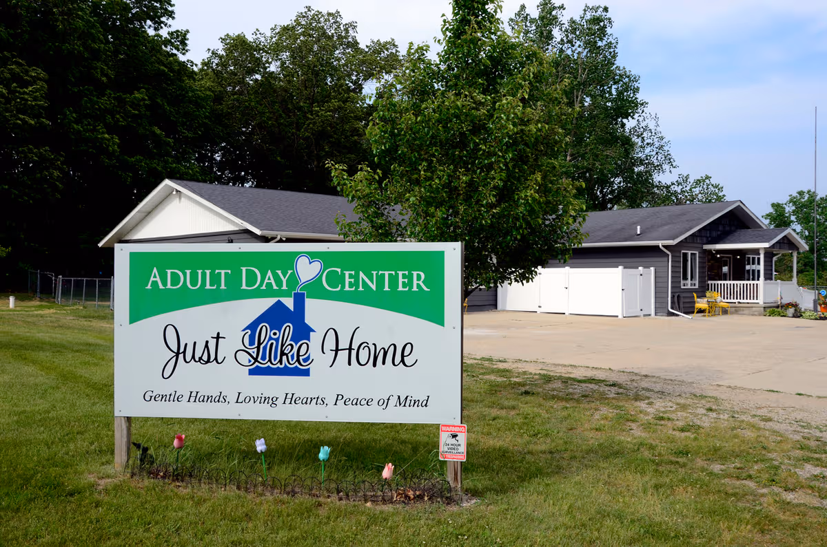 Exterior view of a gray building with a large green and white sign in front.