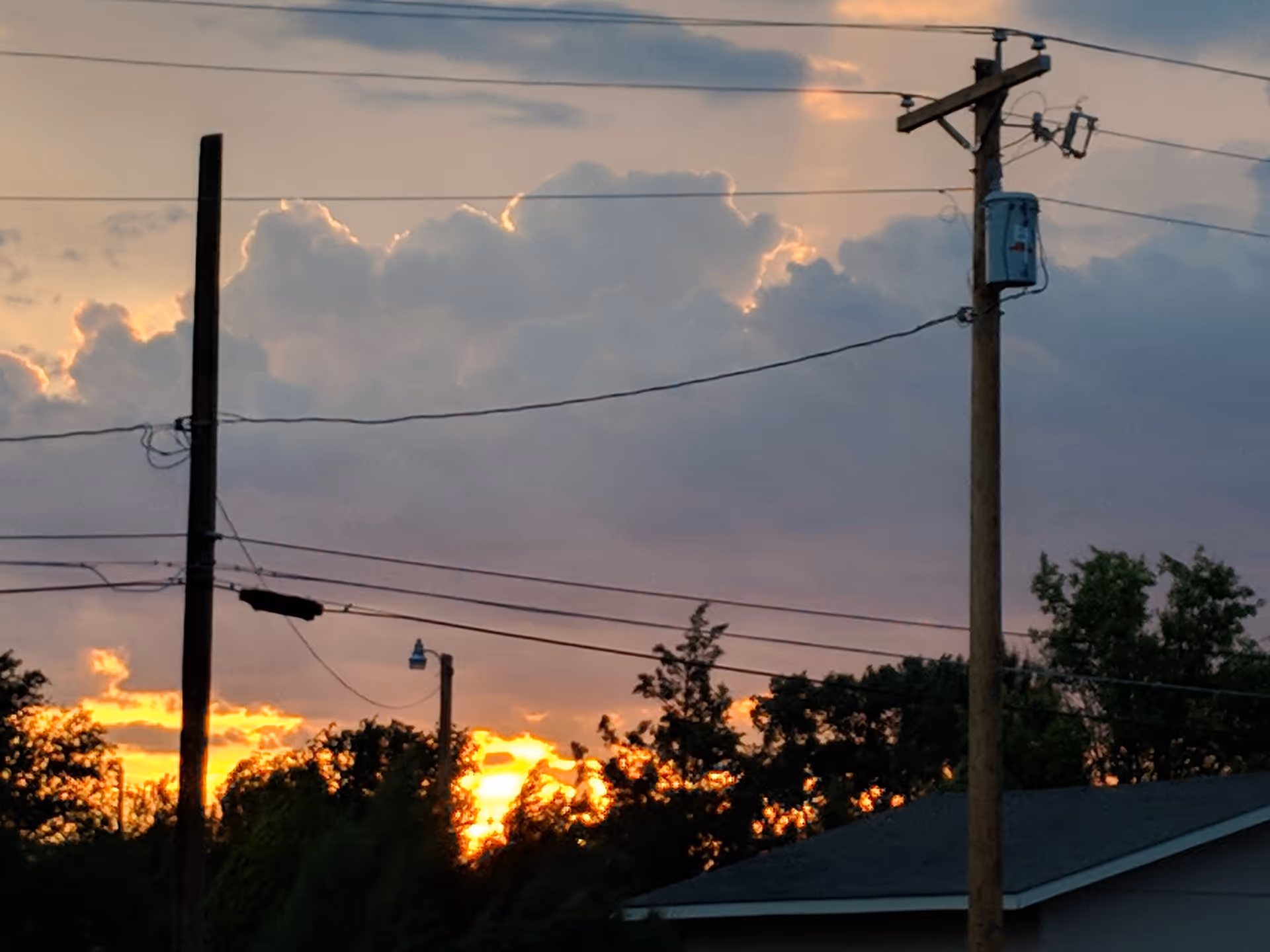 Sunset sky with clouds and utility poles against a residential roofline