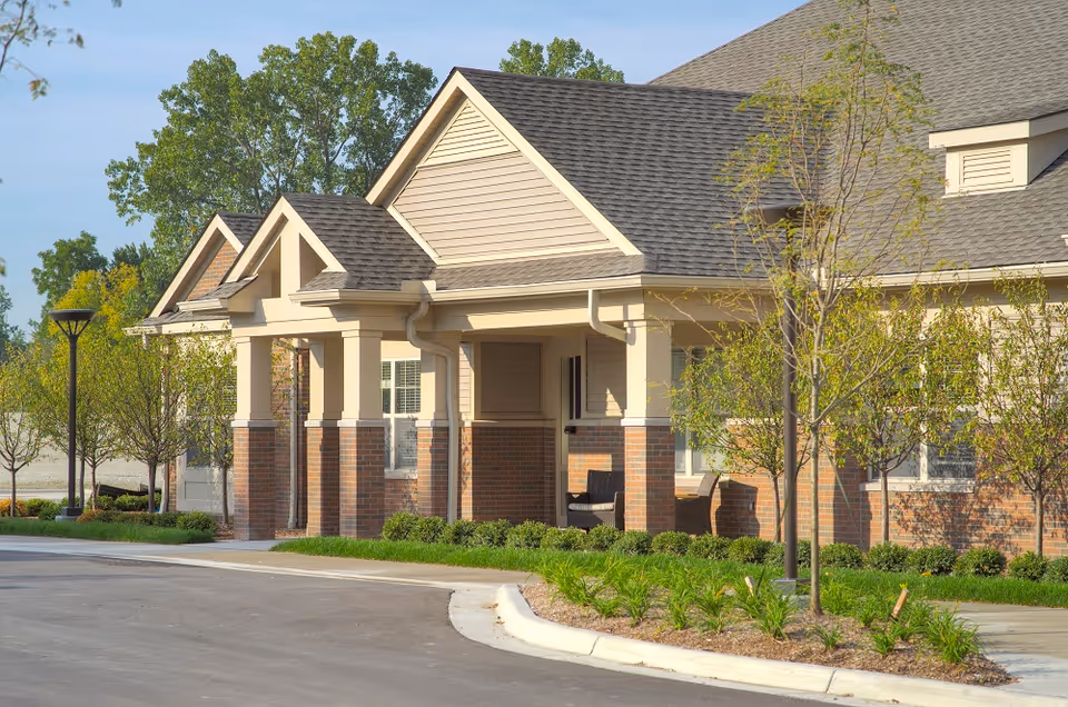 Front exterior of a single-story residential building with covered porches, brick columns and landscaped grounds.
