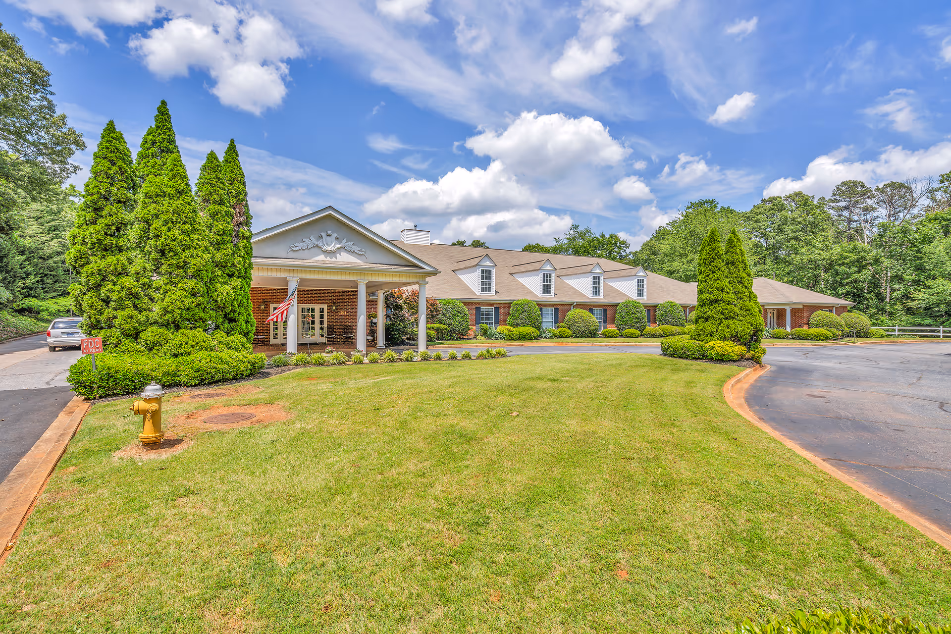Exterior view of Windsor House Greenville with a brick building, manicured lawn, and driveway.